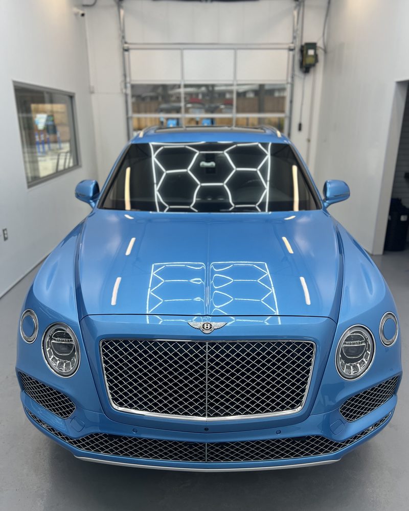 A light blue Bentley Bentayga, bay lights mirrored across the bonnet