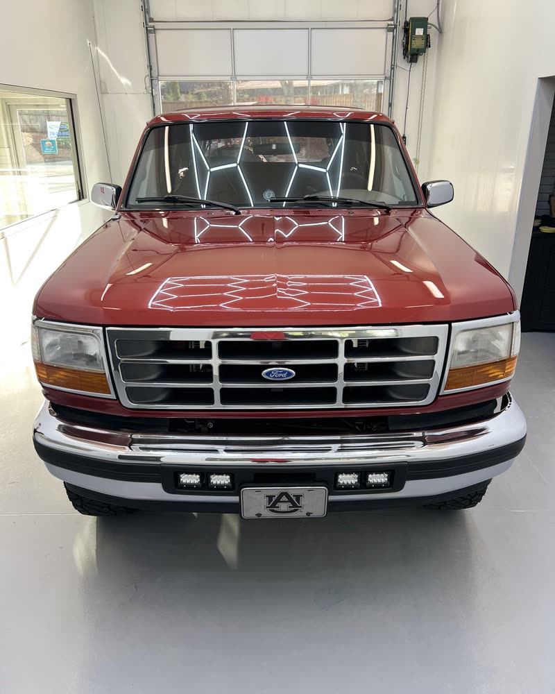 A restored red Ford Bronco, the bay lights held in a deep gloss on the hood