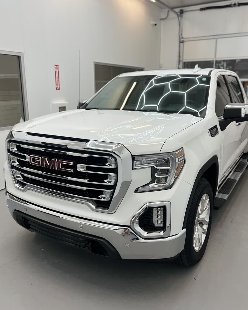 A white GMC Sierra pickup, the bay ceiling lights mirrored across its coated hood