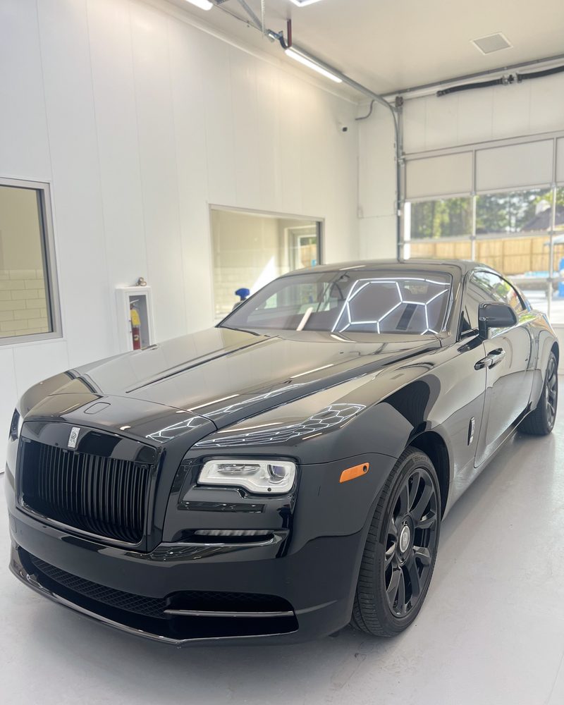 A black Rolls-Royce Wraith, the bay lights reflected along its coated flank