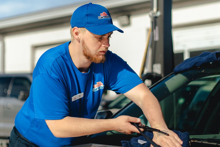 A Mr. Clean team member cleaning the inside of a car's windshield