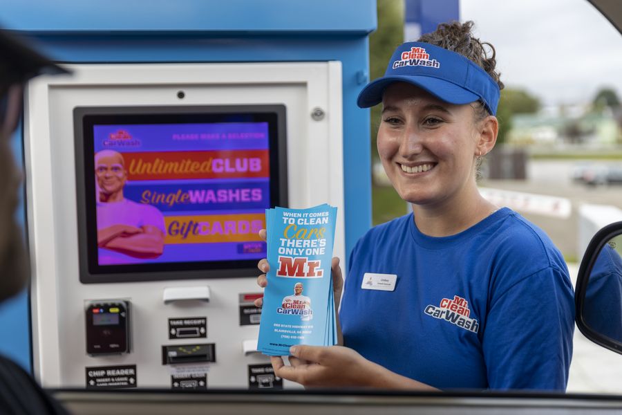Attendant at a Mr. Clean pay station, its screen listing Unlimited Club, Single Washes and Gift Cards